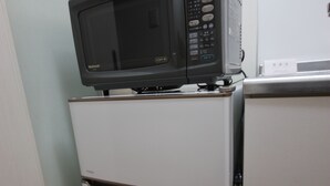 Cocina compacta con un microondas sobre un refrigerador blanco, un electrodoméstico blanco más pequeño a la derecha y piso de madera.