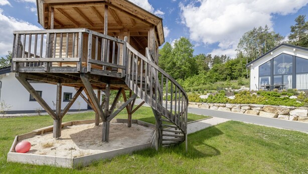 Una struttura in legno con una scala, circondata da un giardino curato e un edificio moderno sullo sfondo.