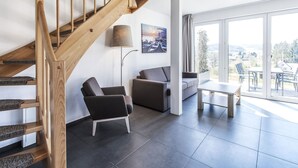 Un soggiorno moderno con una scala in legno, un divano, un tavolino da caffè e una grande finestra con vista sull'esterno.