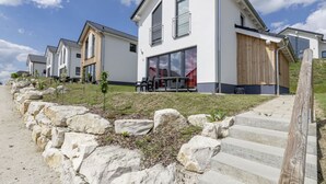 Un edificio residenziale moderno con facciata bianca, ampie finestre e un muro di contenimento in pietra.