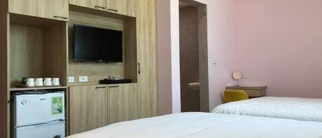 A hotel room with a bed, a television mounted on a wooden cabinet, a refrigerator, and a small table with a lamp.
