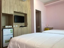 A hotel room with a bed, a television mounted on a wooden cabinet, a refrigerator, and a small table with a lamp.