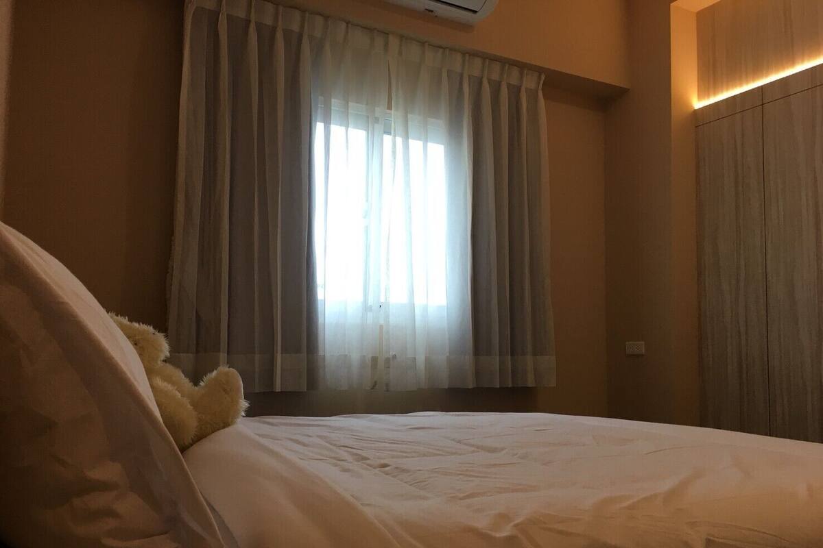 Quarto com cama, janela com cortinas leves e ar-condicionado fixado na parede.