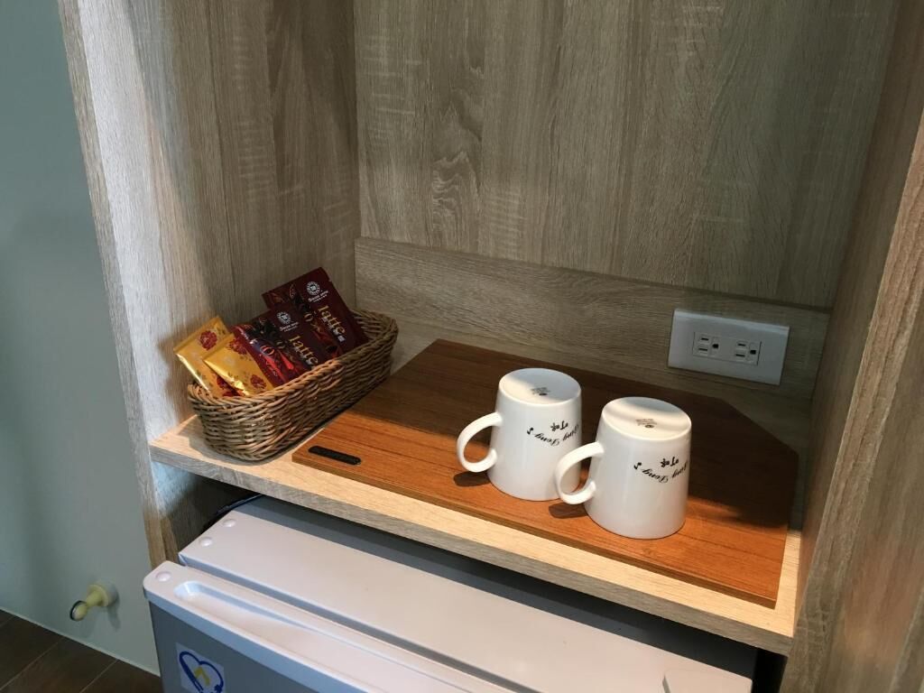 A wooden shelf with two white mugs and a basket of snacks.
