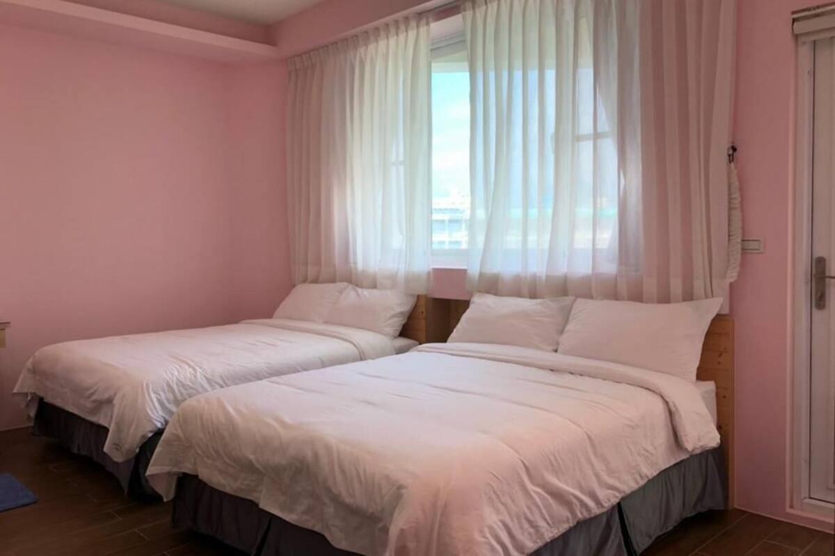 Quarto com duas camas, paredes cor-de-rosa e cortinas leves.