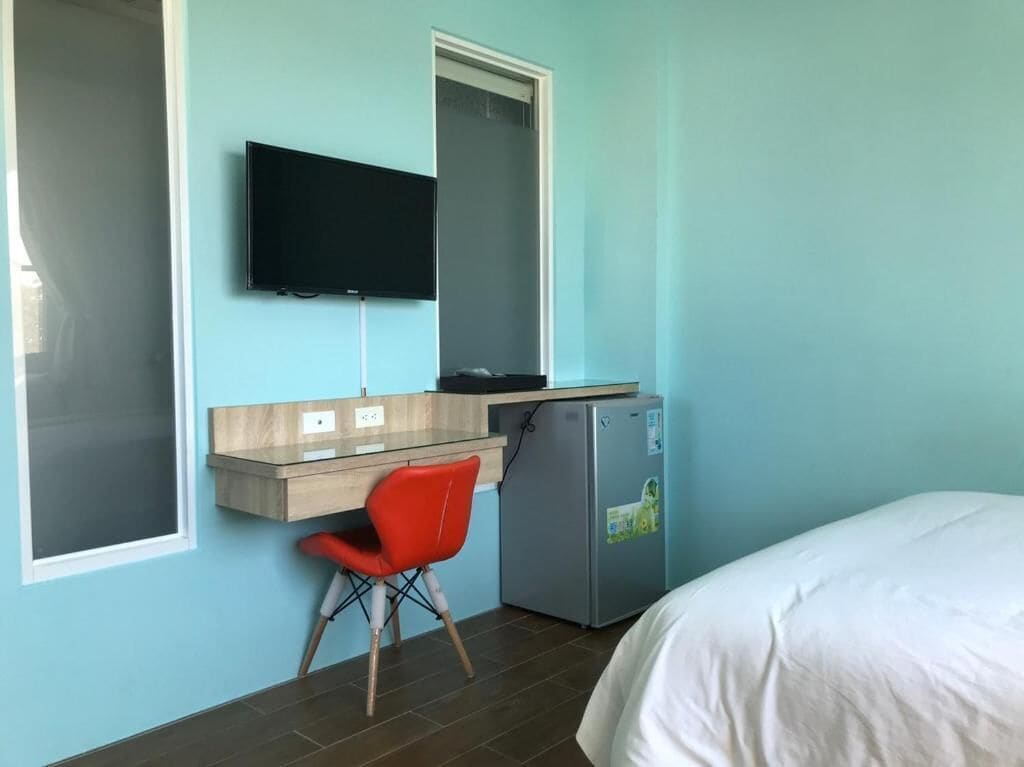 A hotel room with a bed, a desk with a chair, a television, and a refrigerator.