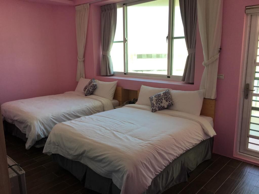 A room with two beds, each with a pillow and a window with curtains.