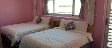A room with two beds, each with a pillow and a window with curtains.