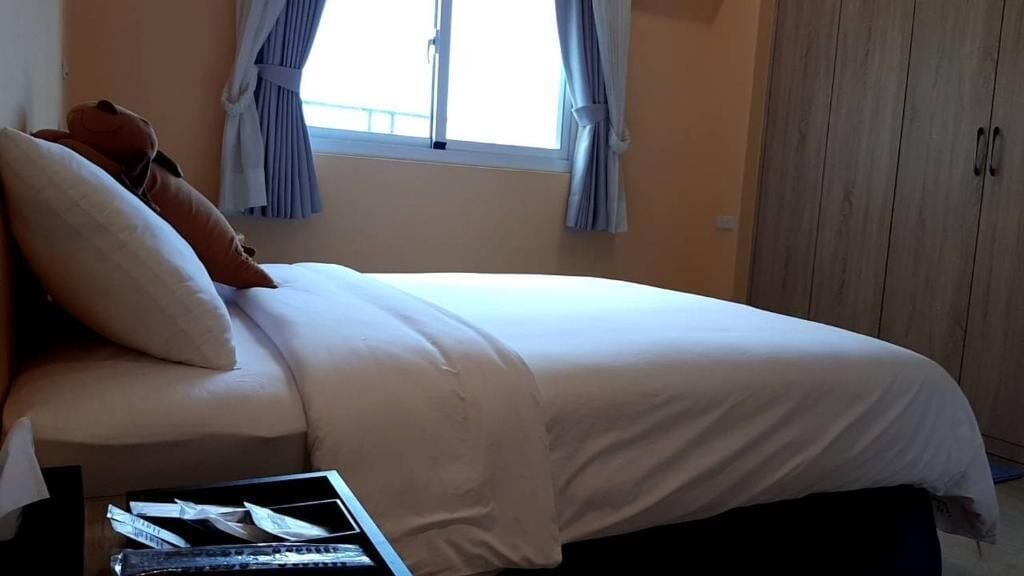 Un dormitorio con cama, mesita de noche, ventana con cortinas y armario.