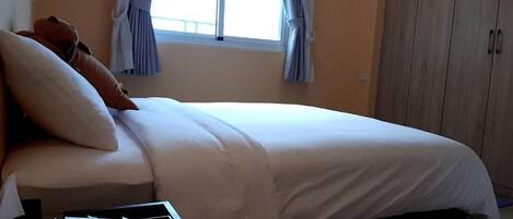 A bedroom with a bed, a nightstand, a window with curtains, and a wardrobe.