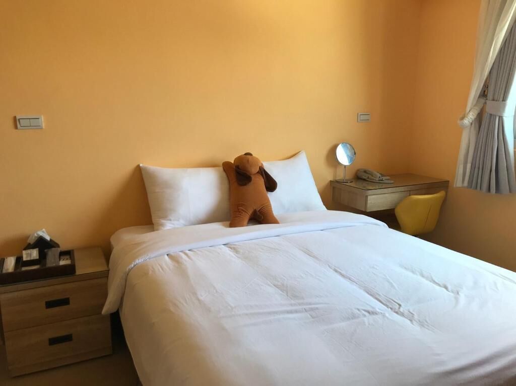 A hotel room with a bed, a nightstand, a chair, and a window with curtains.