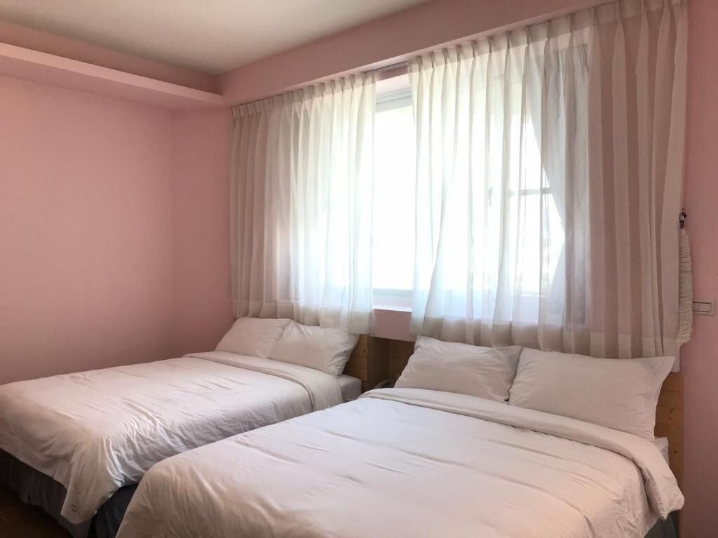 Une chambre avec deux lits, une fenêtre avec des rideaux légers et une lampe de chevet.