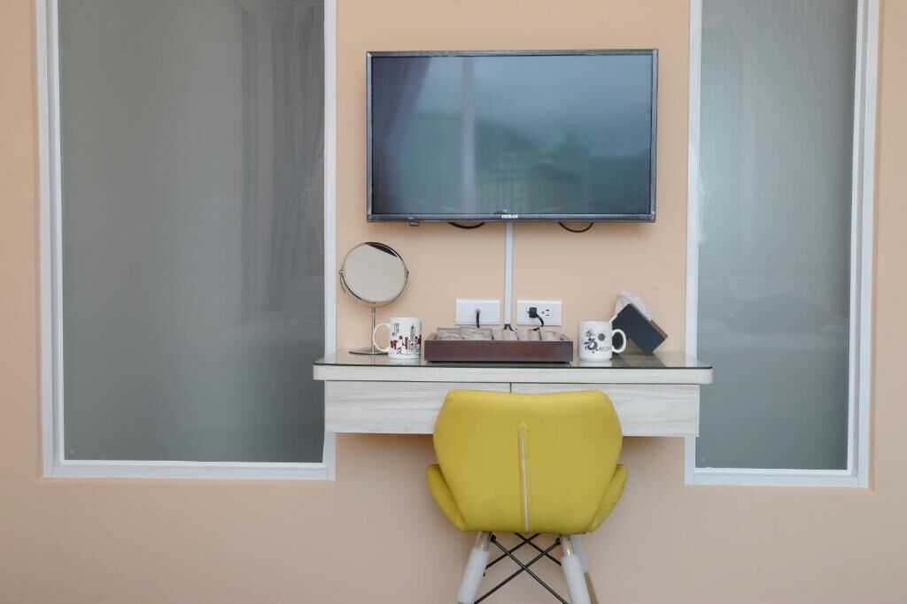 A small, modern room with a desk, a yellow chair, a television, and a window.