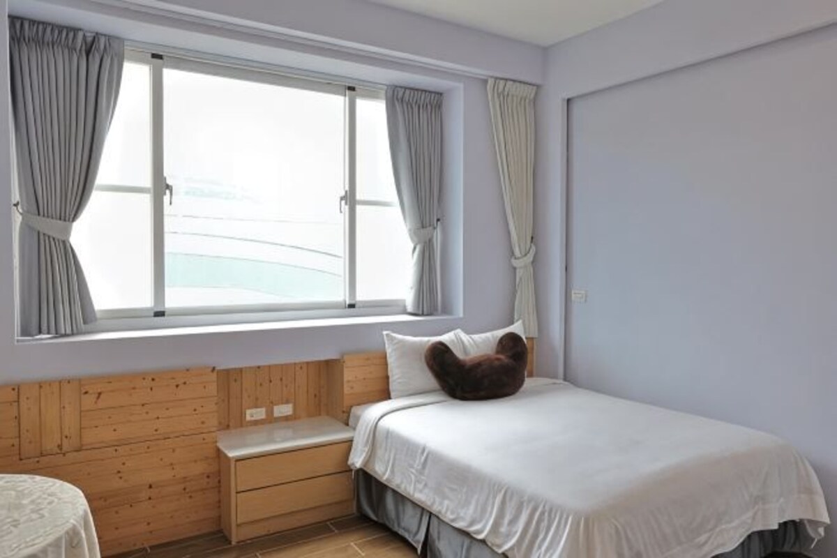 Une chambre à coucher avec un lit, un banc en bois, une fenêtre avec des rideaux et une vue sur la mer.