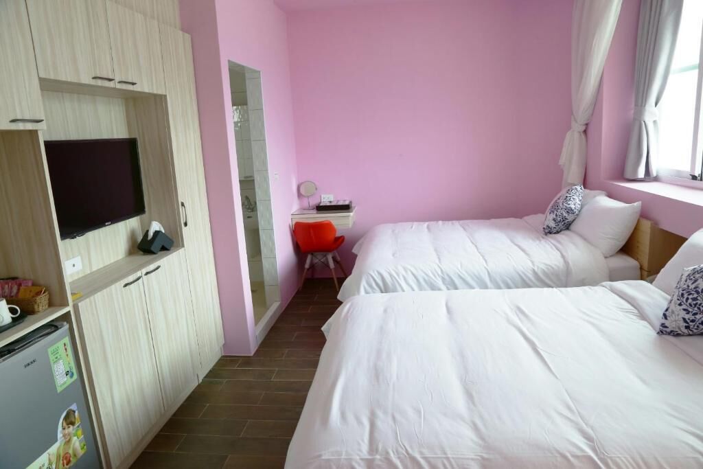 Quarto com duas camas, uma escrivaninha com cadeira, televisão e guarda-roupa.