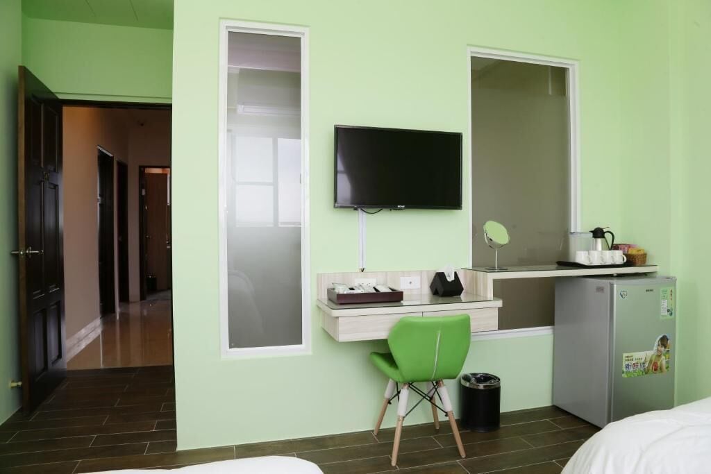 A room with a bed, a desk with a chair, a television, a refrigerator, and a trash bin.