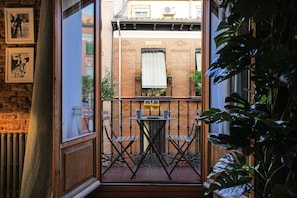 A balcony with a table and chairs, a view of a brick building, and potted plants. - Tirso Design II (Madrid)