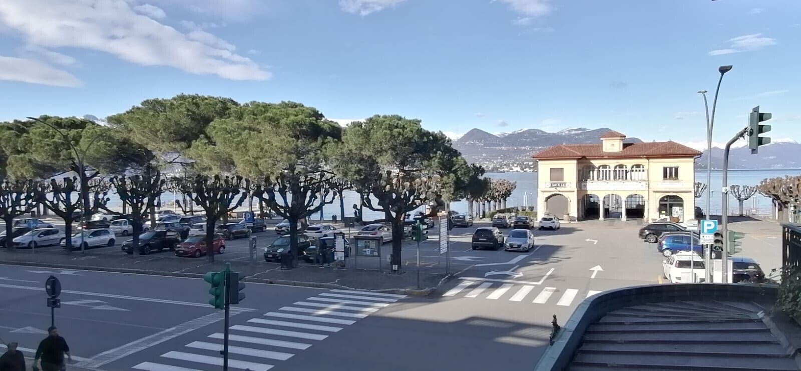 Una strada costiera con auto parcheggiate, un attraversamento pedonale e un edificio con un portico.