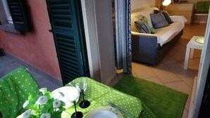 Uma área de refeições com uma mesa posta para dois, toalha de mesa verde e um vaso com flores brancas.