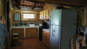 Een landelijke keuken met houten kastjes, een koelkast, een fornuis en een raam boven de spoelbak.