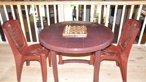 A round wooden table with a chessboard in the center, surrounded by two red plastic chairs. - Water View Holiday Retreat (Belur)