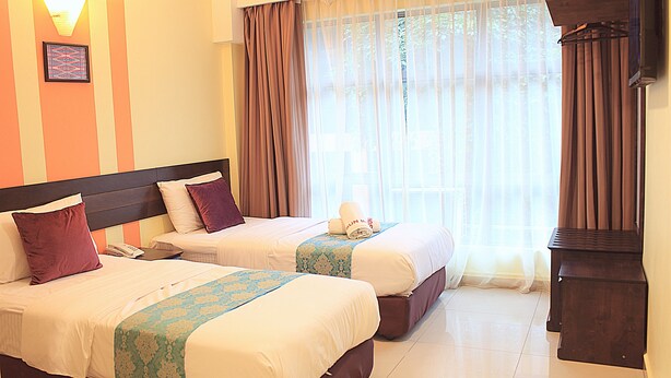 Habitación de hotel con dos camas, una mesita de noche, una lámpara y una ventana con cortinas.