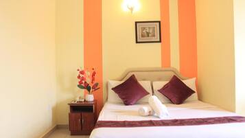 A hotel room with a bed, pillows, a nightstand, a vase with flowers, and a framed picture on the wall.