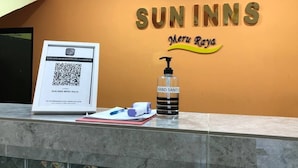 Una zona de recepción con un código QR para el registro, una botella de gel hidroalcohólico y un letrero que dice "SUN INNS MERU RAYA".