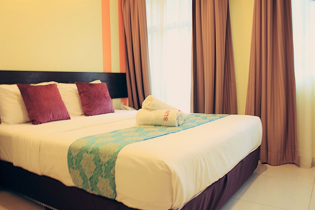 A hotel room with a bed, pillows, a headboard, curtains, and a window.