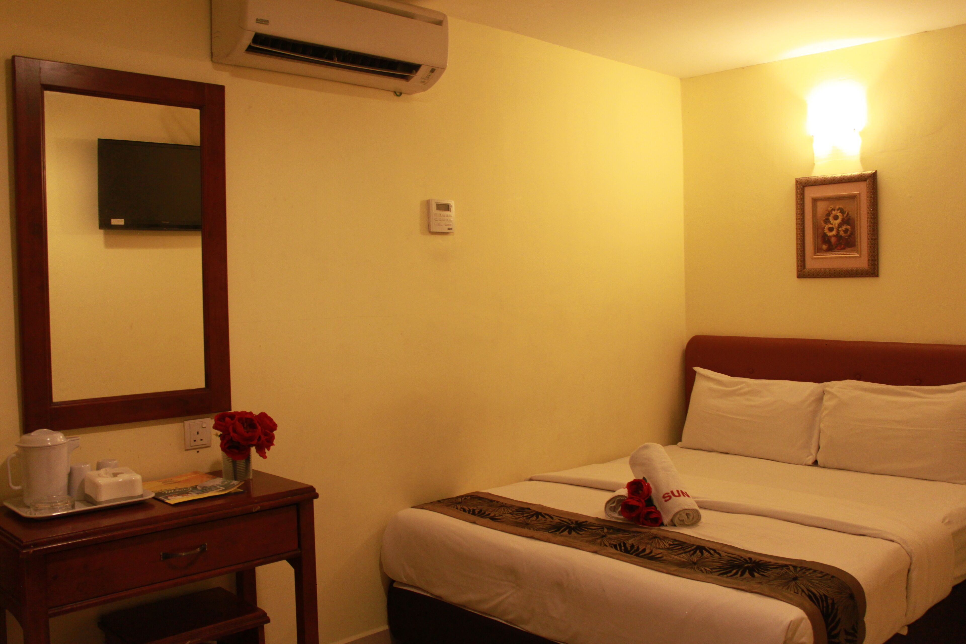 A hotel room with a bed, a bedside table with a lamp, a mirror, and a wall-mounted air conditioner.