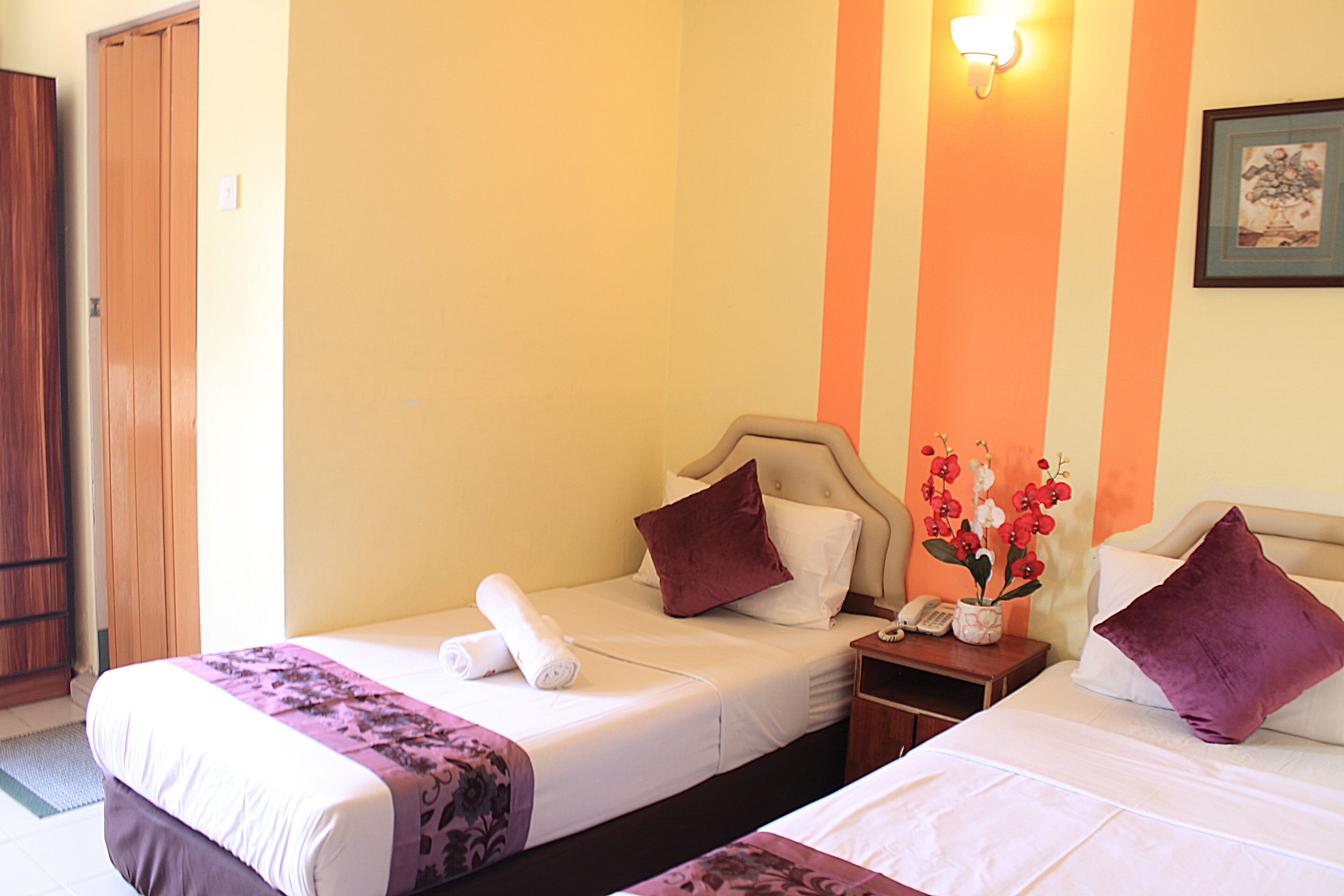 A hotel room with two single beds, a wooden wardrobe, a nightstand with a phone, and a wall-mounted light fixture.
