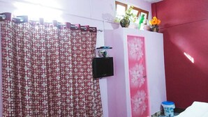 A bathroom with a patterned shower curtain, a pink door, and a small black speaker on the wall. - Kaziranga   homestay (Kohora)