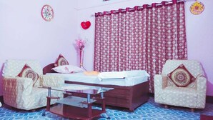 A bedroom with a bed, two armchairs, a small table, and a curtain. - Kaziranga   homestay (Kohora)