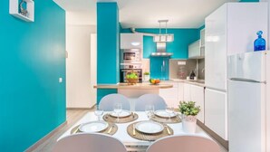 A modern kitchen with teal walls, white cabinets, and a dining area set for four with round tables and plates. - Gran Reserva by Interhome (Empuriabrava)