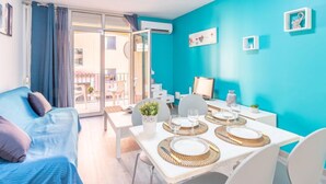 A bright room with a teal wall, a dining table set with plates and glasses, a sofa with cushions, and a view through a glass door to an outdoor area. - Gran Reserva by Interhome (Empuriabrava)