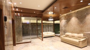 A modern lobby with a marble floor, a beige sofa, and a glass elevator. - Hotel Cliffton (Mumbai)