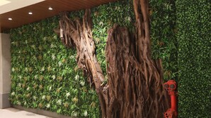 A wall with vertical wooden trunks and a green leafy backdrop. - Hotel Cliffton (Mumbai)