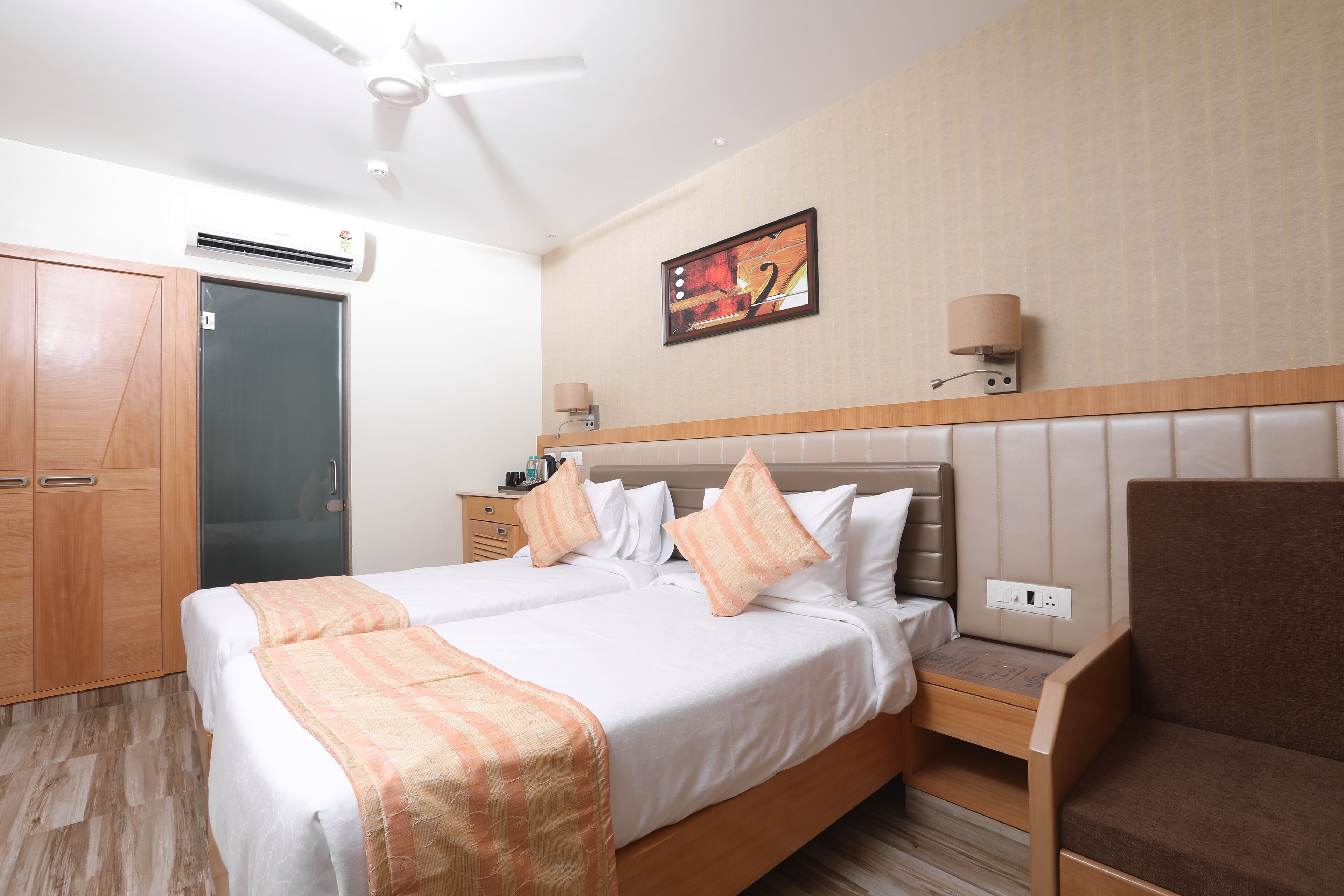 Ein Hotelzimmer mit Bett, Stuhl, Nachttisch, Wandlampe und Klimaanlage.