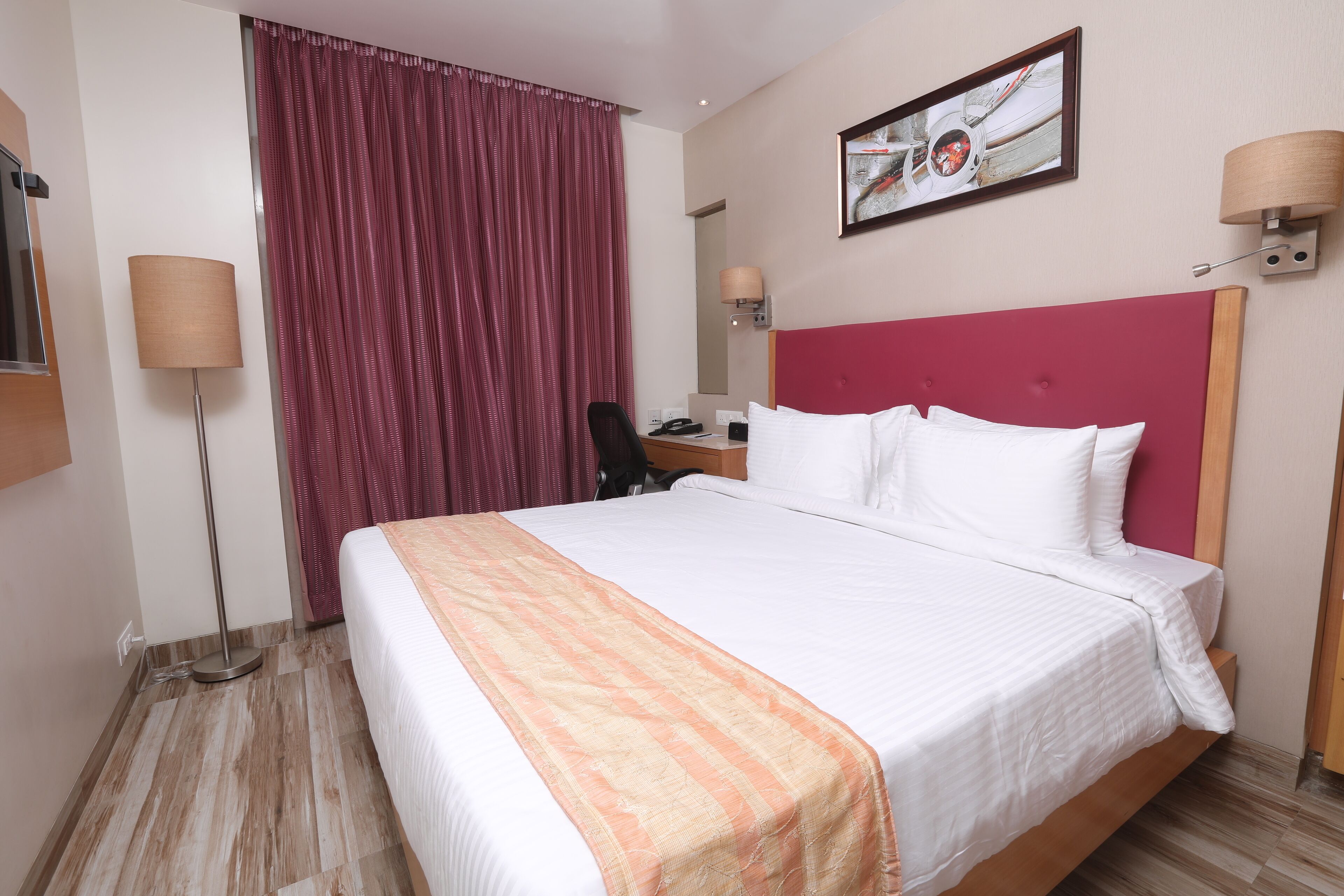 A hotel room with a large bed, a desk, a chair, a lamp, and a window with curtains.