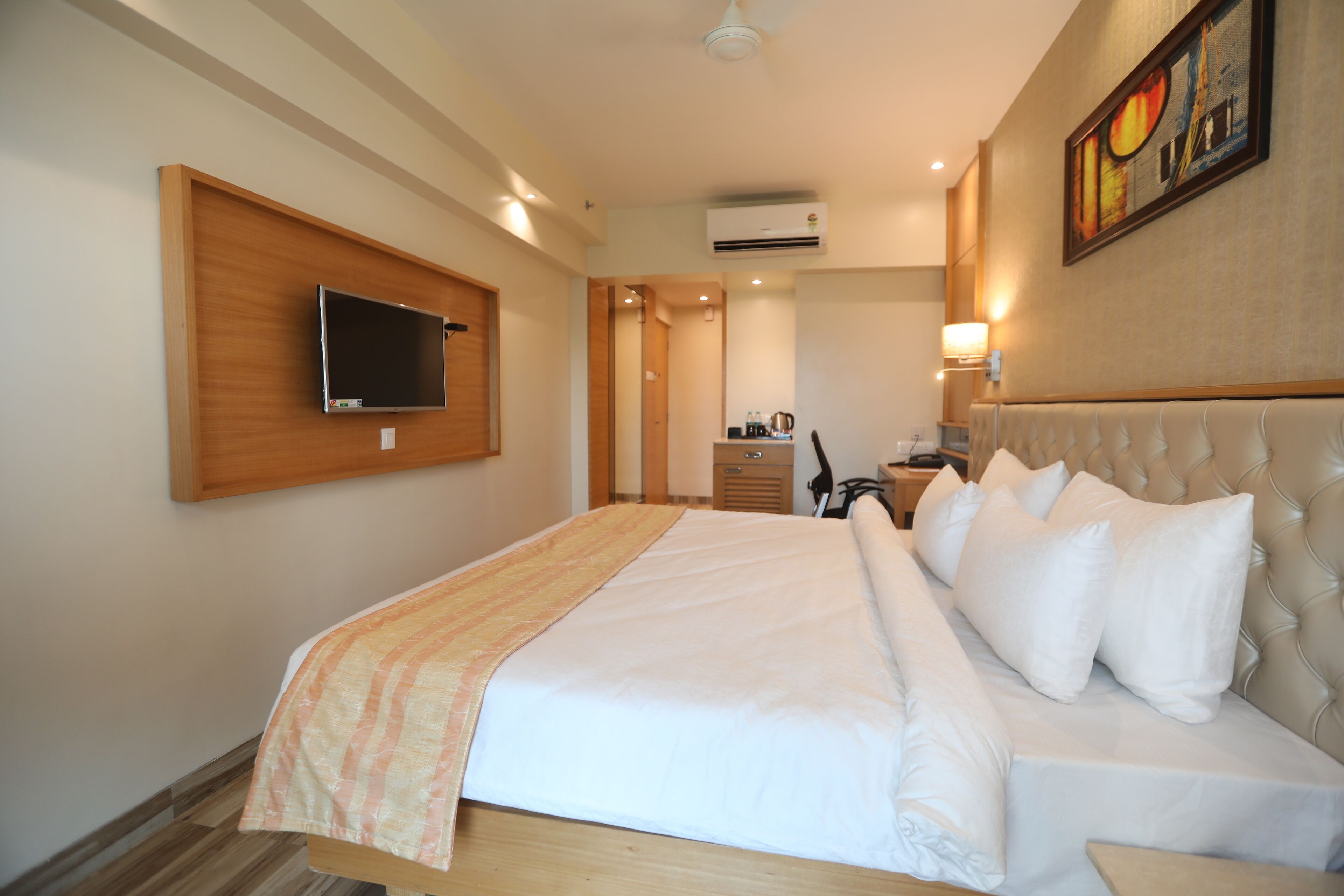 Habitación de hotel con una cama grande, un televisor de pantalla plana montado en la pared, un escritorio con una silla y un equipo de aire acondicionado.