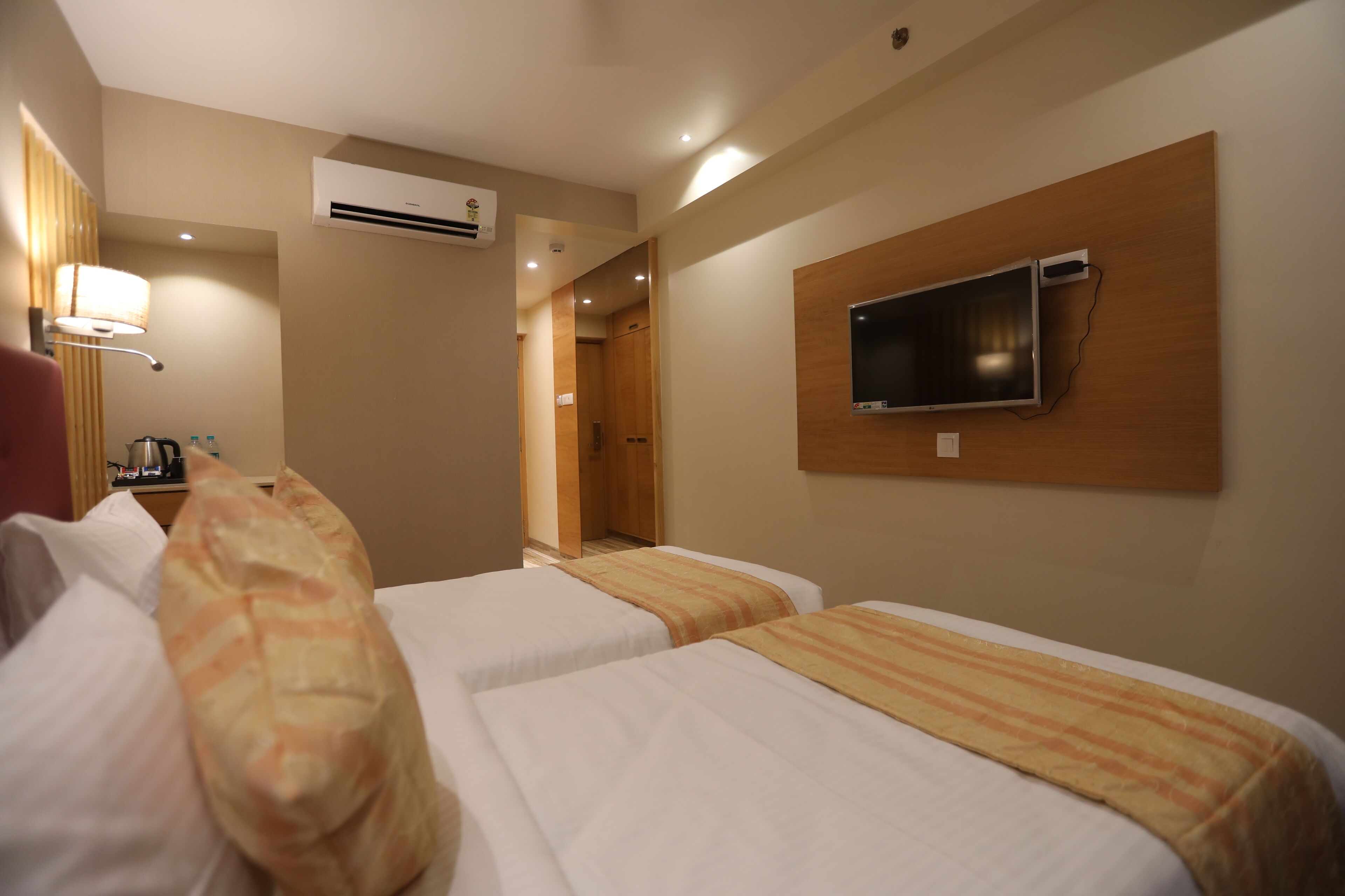Une chambre d’hôtel avec deux lits, un téléviseur fixé au mur, un appareil de climatisation et une lampe.