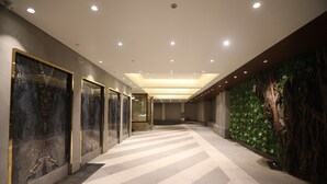 A hallway with a patterned floor, recessed lighting, and a wall with a green leafy design. - Hotel Cliffton (Mumbai)