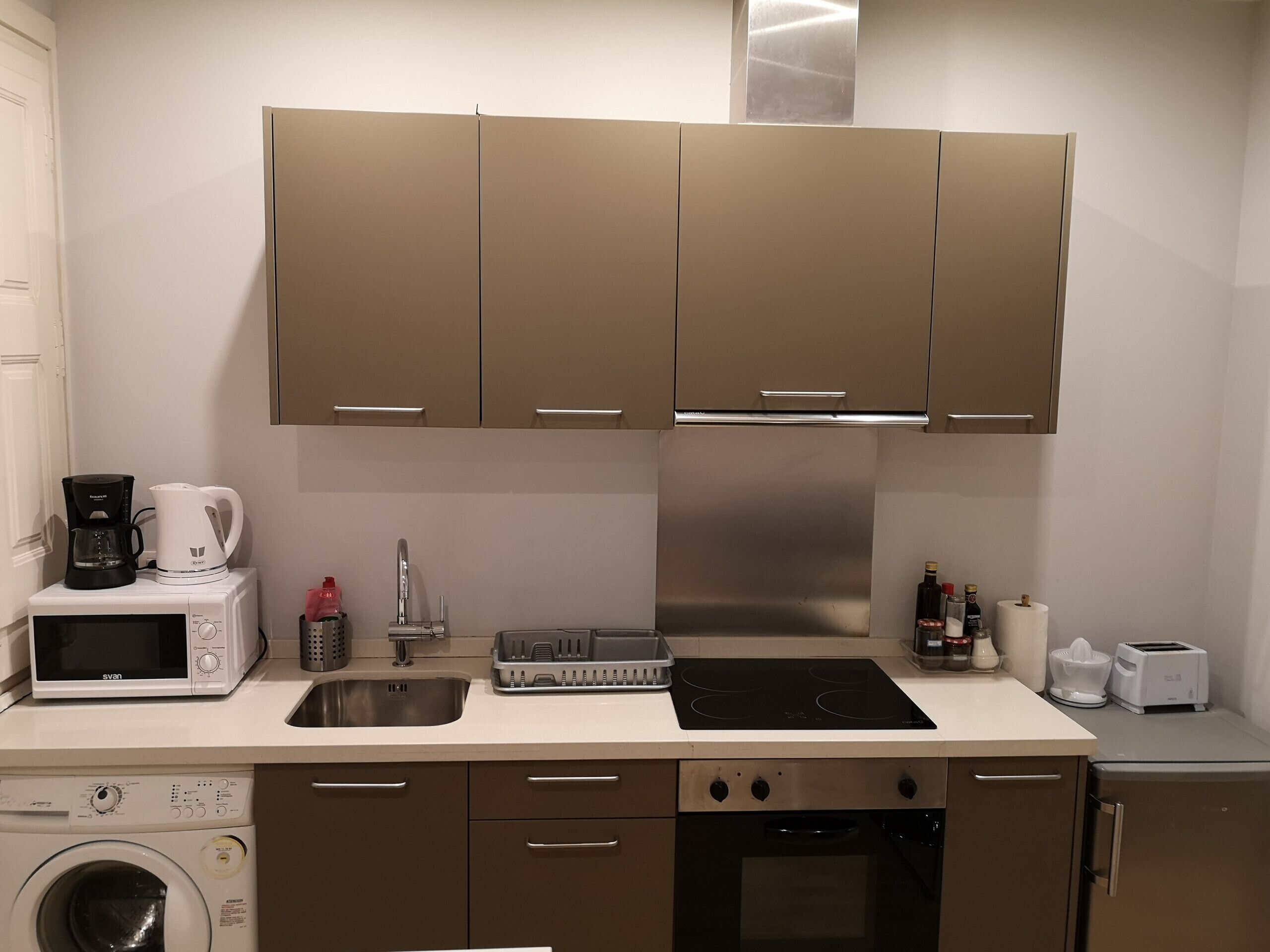 Une cuisine compacte équipée d’un four à micro-ondes, d’un grille-pain, d’un évier, d’une cuisinière et d’un lave-linge.