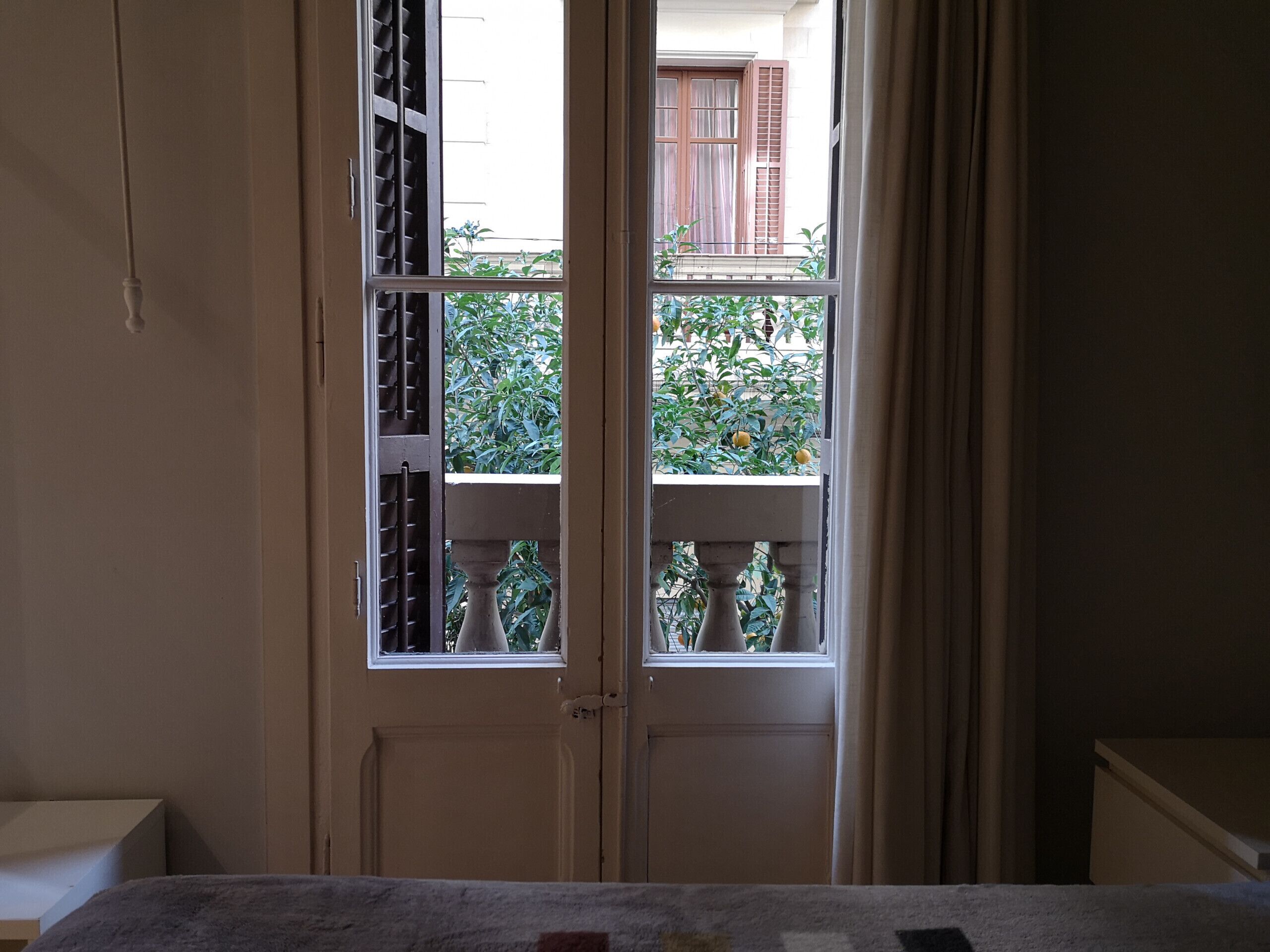 A room with a door leading to a balcony with a view of greenery and a building.