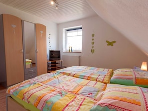 A bedroom with two beds, a wardrobe, a television, and a window with a view.