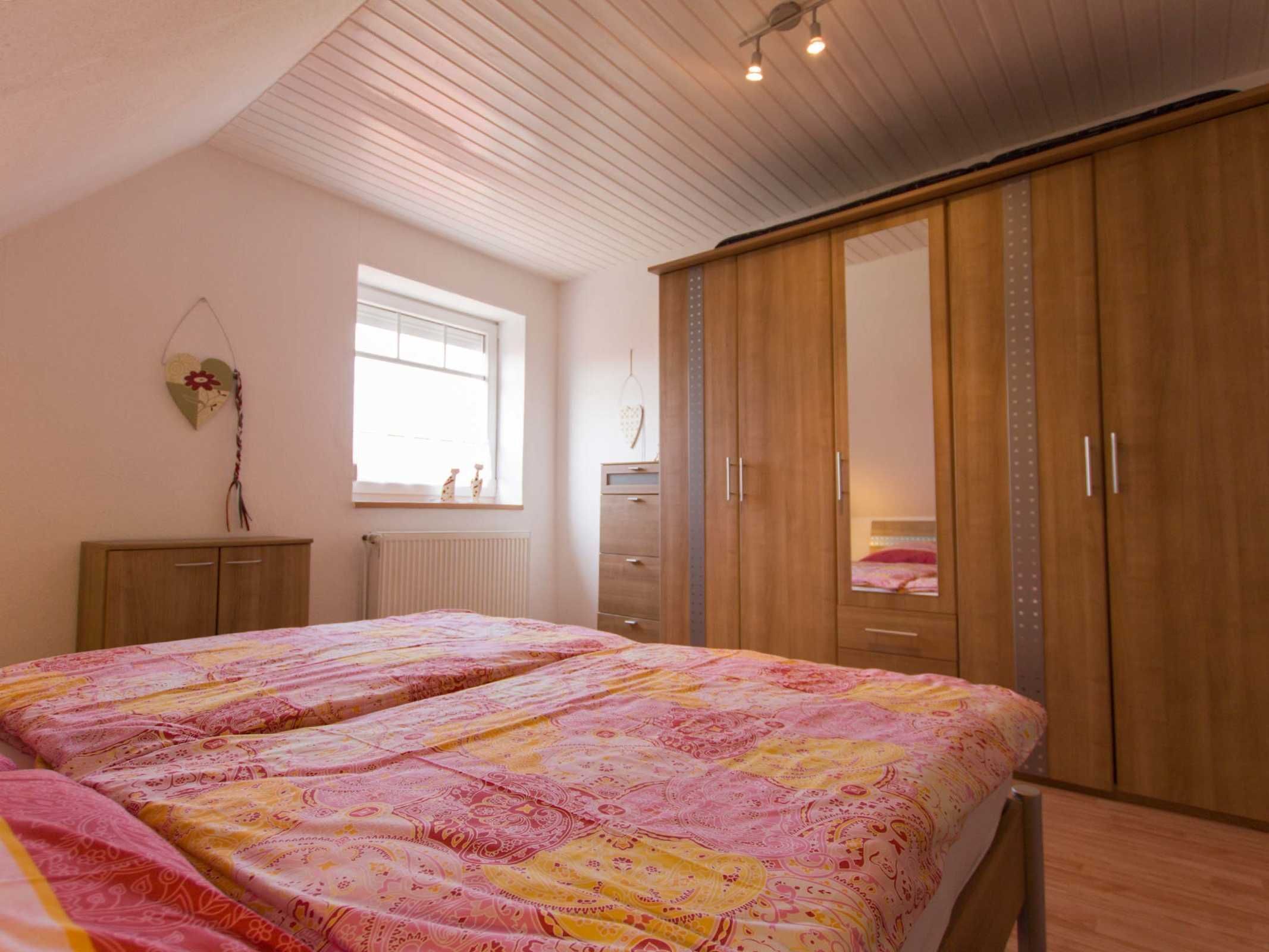 Une chambre à coucher avec un grand lit, une armoire, une commode, un radiateur et une fenêtre.