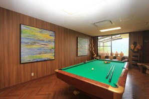 A pool table with a green felt surface, surrounded by wooden walls and two large paintings. - Harriway Hotel Hakone (Hakone)