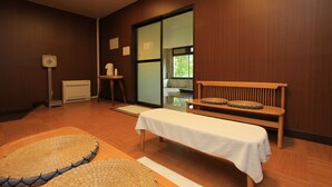 Ein Zimmer mit einer hölzernen Bank, einem kleinen Tisch mit weißem Tuch, einer gewobenen Matte und einem Heizgerät.