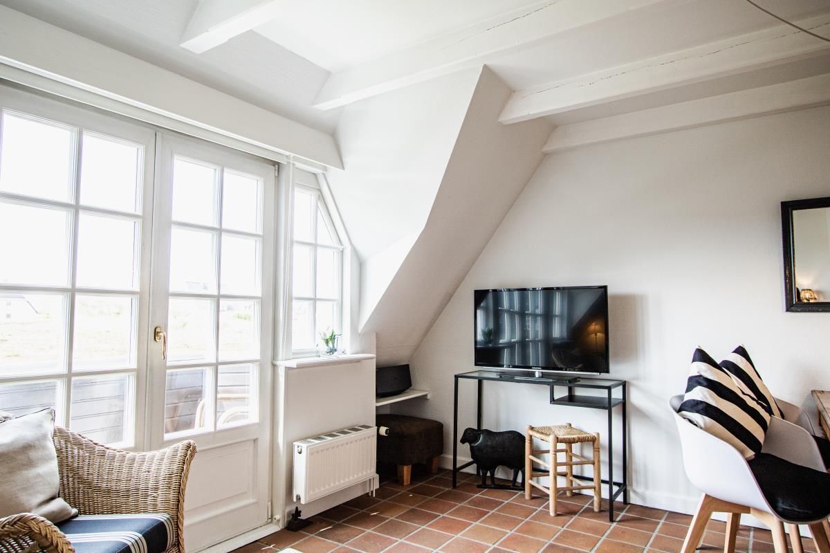 Una habitació acollidora amb una finestra gran, un televisor sobre un suport, un sofà i una cadira.
