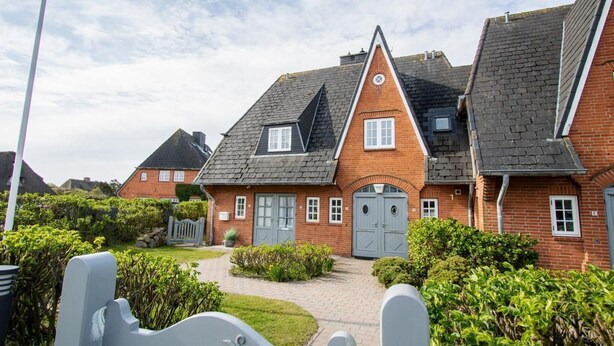 Eine Reihe von roten Backsteinhäusern mit grauen Dächern, einem zentralen Eingang und einem gepflegten Garten.